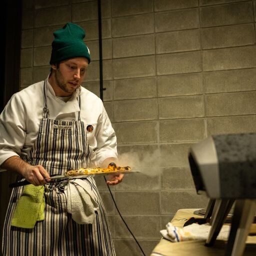 Cheflon in chef hat and apron at outdoor cooking setup — private pizza chef